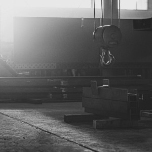 Lichtdurchflutete Werkhalle von Rewesta Metallbau mit schwebendem Kranhaken und schweren Stahlprofilen auf dem Hallenboden.