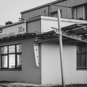 Gesamtansicht des Eingangsbereichs von Rewesta Metallbau mit Firmenschild, markantem Vordach aus Stahlträgern und großen Fenstern zur Straße.