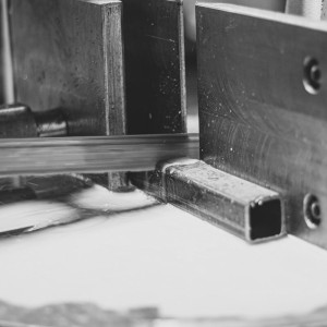 Nahaufnahme einer Metallbandsäge beim Zuschnitt eines rechteckigen Stahlprofils unter Kühlmittelfluss in der Werkstatt von Rewesta Metallbau.