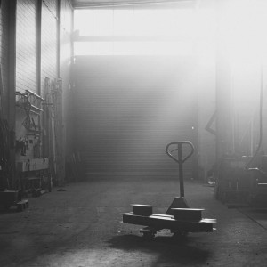 Lichtdurchflutete Werkhalle mit geschlossenem Rolltor bei Rewesta Metallbau, im Vordergrund ein Hubwagen mit Metallteilen, Werkzeuge an der Wand.